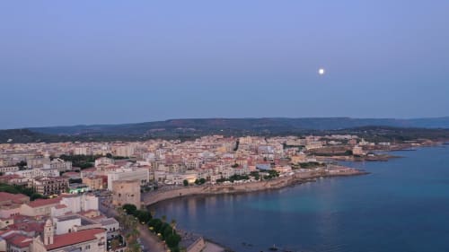 Vista aerea al tramonto di Alghero con porto, mare Mediterraneo e luna che sorge sui colli della Sardegna