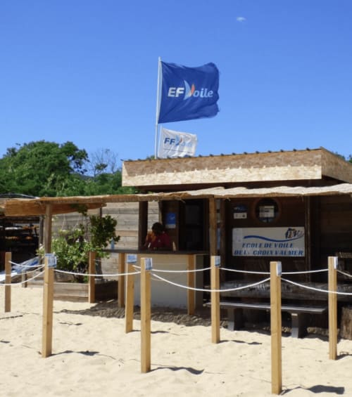 Bâtiment de l'école de voile EF Voile avec drapeaux sur la plage de sable à La Croix Valmer