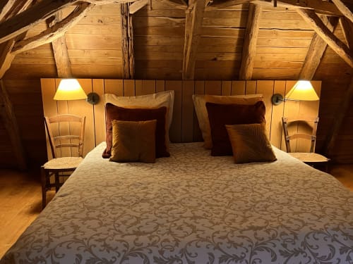Chambre rustique sous les combles de la chaumière Le Lapin sur le Toit avec lit queen-size, oreillers bordeaux, lampes de chevet et poutres apparentes