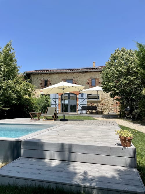 Villa en pierre rustique avec piscine et terrasse bois à Montaut. Cour ensoleillée avec parasols, transats et jardins aménagés