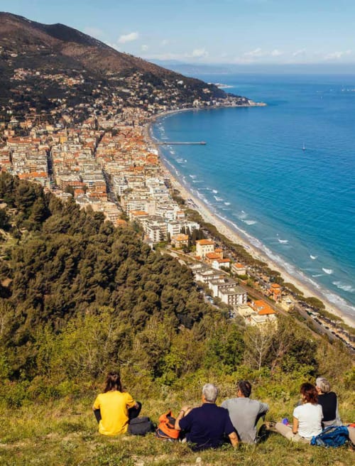 Visitors enjoy scenic viewpoint overlooking Hotel Beau Rivage and Alassio's coastal beach nestled between forested hills and