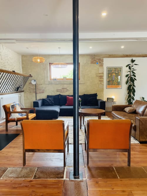 Modern open-plan living area at Maison Monsieur Léger with orange chairs, black sofa, and wooden finishes in Montaut