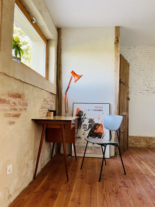 Cozy desk workspace at Maison Monsieur Léger with orange lamp, chair, and vintage posters in Montaut