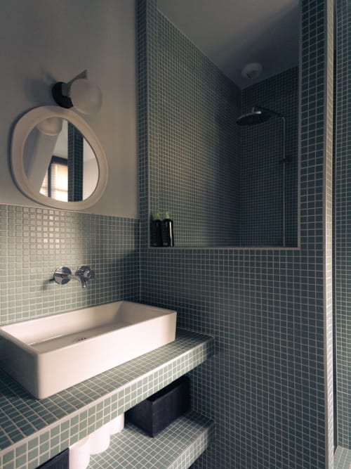 Salle de bain moderne de la chambre Colette à La Guirtelle avec carrelage mosaïque turquoise, lavabo blanc, miroir rond et douche à l'italienne