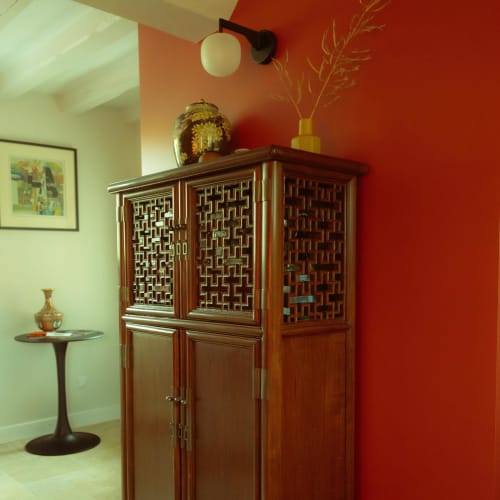 Meuble asiatique en bois aux portes grillagées décoratives dans la chambre rouge de La Guirtelle, agrémenté d'un vase ornemental