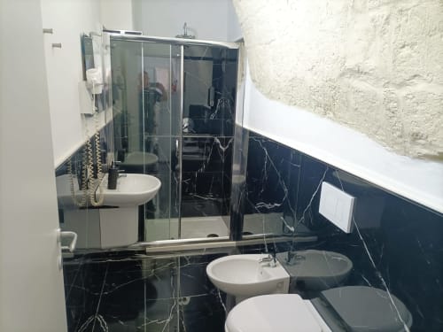Bagno moderno dell'hotel Newhouse Bari con piastrelle in marmo nero, box doccia in vetro, doppi lavandini e finiture bianche