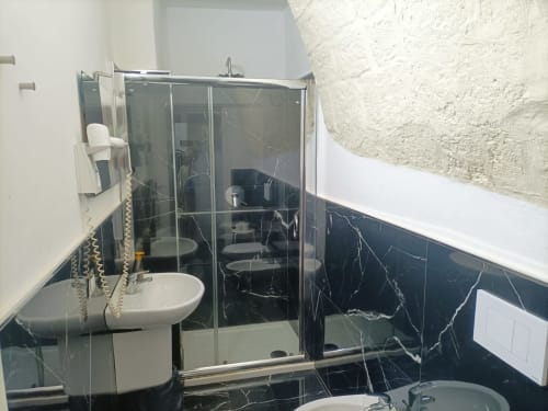 Bagno moderno dell'hotel Newhouse a Bari con piastrelle in marmo nero, box doccia in vetro, lavabo e sanitari bianchi.