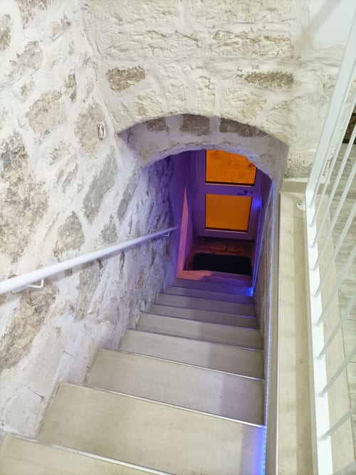 Vano scale di Newhouse Bari con gradini illuminati in viola che conducono a una porta con cornice arancione