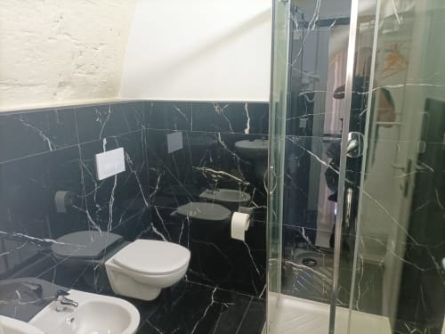 Modern black marble bathroom at Newhouse hotel in Bari with white toilet, sink, and glass shower enclosure