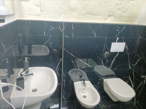 Modern bathroom at Newhouse Bari hotel with black marble tiles, white fixtures including sink, bidet, and toilet