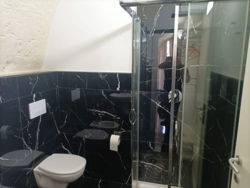 Modern bathroom at Newhouse hotel in Bari with black marble tiles, white toilet, glass shower enclosure, and city views