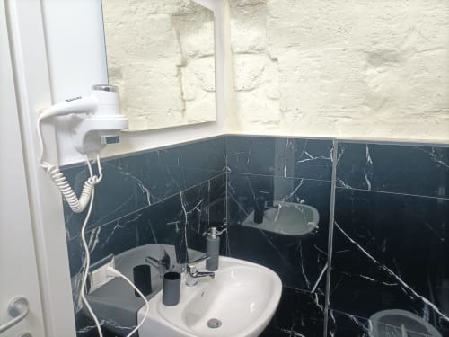 Modern bathroom at Newhouse hotel in Bari with white sink, black marble tile backsplash, wall-mounted hairdryer, and bathroom