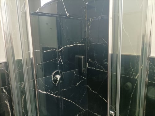 Damaged black marble shower enclosure at Newhouse hotel in Bari with cracked glass panels
