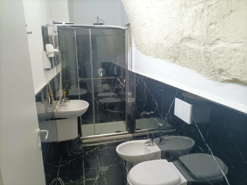 Modern bathroom at Newhouse hotel in Bari with black marble tiles, shower enclosure, and white fixtures