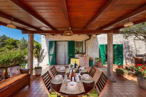 Terrazza coperta della Villa Margherita con tavolo preparato, travi in legno, persiane verdi e vista sul giardino a Santeramo