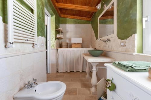 Bagno elegante a Villa Margherita con pareti verdi, finiture bianche, lavabo su colonna e travi in legno