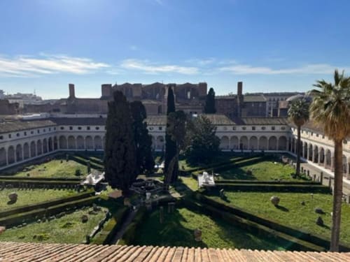 Cortile della Michelangelo Suite Roma con giardini curati, cipressi e rovine romane storiche che si affacciano sulla città.