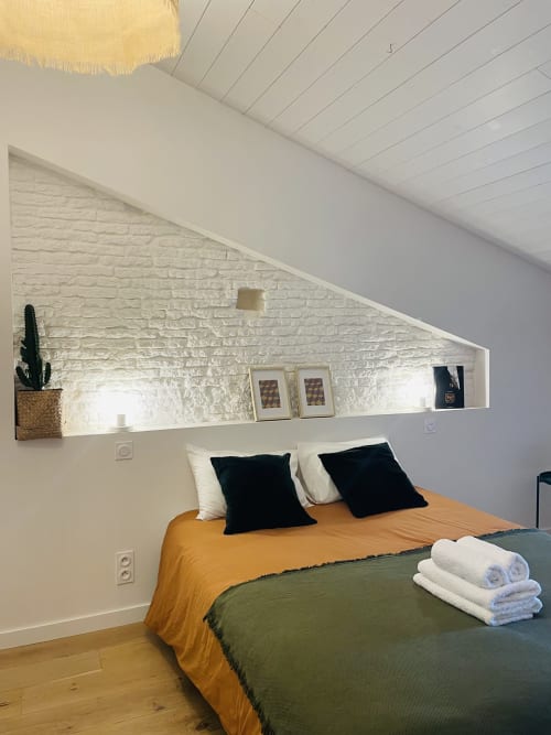 Chambre accueillante à la Maison Monsieur Léger avec literie jaune, oreillers noirs, plafond mansardé et étagères intégrées décorées