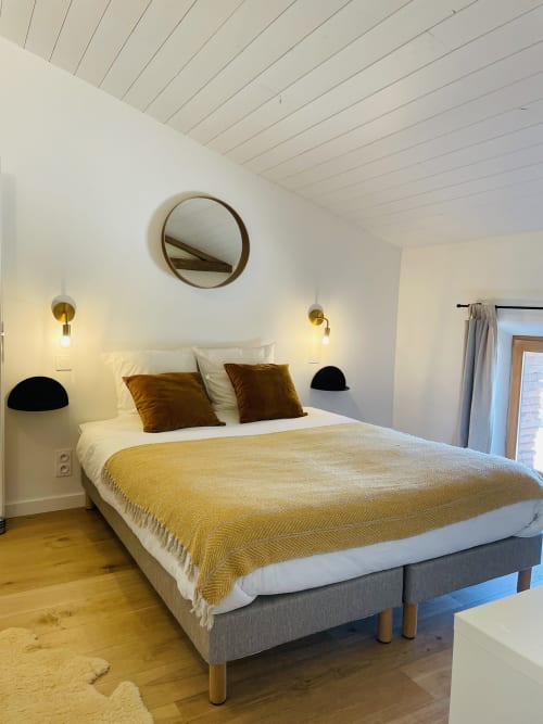 Chambre élégante avec plaid jaune, touches dorées, plafond blanc géométrique et miroir rond à Maison Monsieur Léger