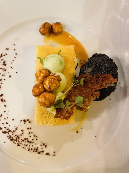 Gourmet plated dessert at Maison Monsieur Léger featuring sponge cake, caramelized nuts, green apple, and dark crumb garnish