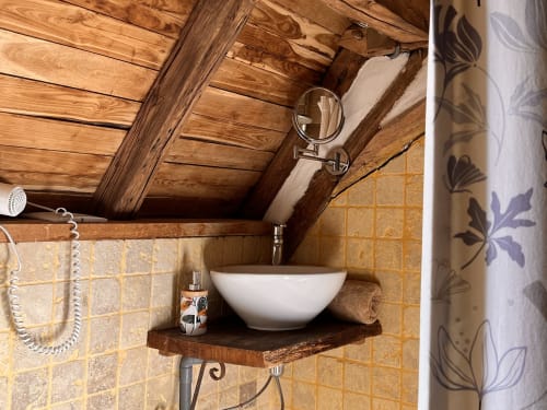 Salle de bain rustique du Lapin sur le Toit avec poutres en bois, vasque blanche sur étagère bois et murs en carreaux terracotta