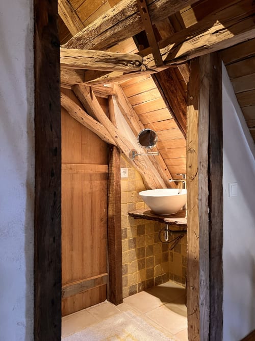 Salle de bains rustique au Lapin sur le Toit avec poutres en bois apparentes, vasque blanche et murs carrelés à Rouffignac, France.