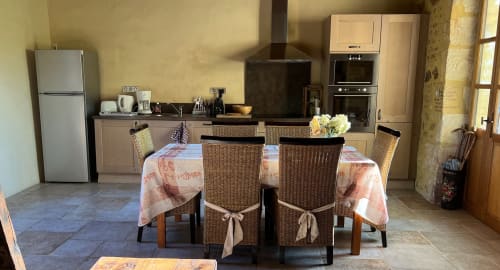 Espace cuisine-salle à manger du gîte Le Lapin sur le Toit à Rouffignac avec table ronde, chaises en rotin et électroménagers modernes