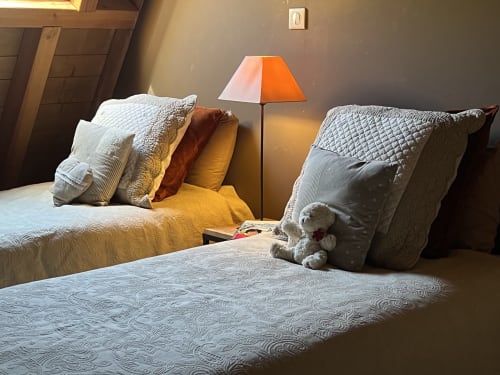 Chambre accueillante au gîte Le Lapin sur le Toit à Rouffignac avec deux lits, oreillers matelassés et lampe de chevet orange