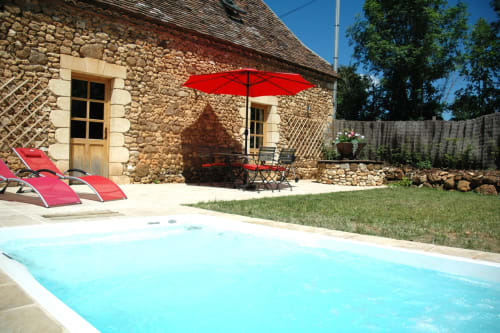 Piscine et cour en pierre du gîte Le Lapin sur le Toit avec parasol rouge, Rouffignac, France