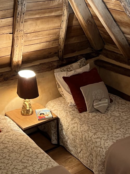 Chambre chaleureuse du gîte Le Lapin sur le Toit avec poutres apparentes, lit à la literie motifs, table de nuit bois