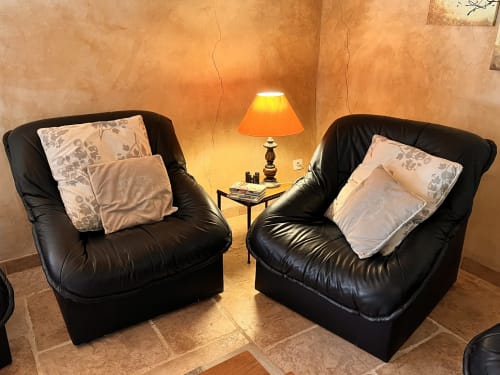 Coin salon cosy du gîte Le Lapin sur le Toit avec deux fauteuils noirs en cuir, coussins décoratifs et lampe chaleureuse