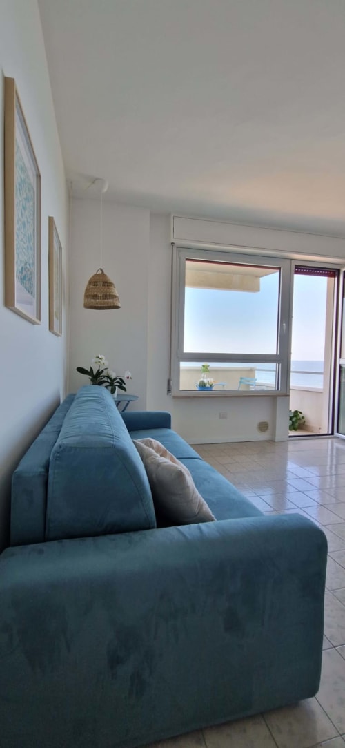 Bright seafront apartment living room with blue sofa, sea view through large window, and modern furnishings at Lamar Suites