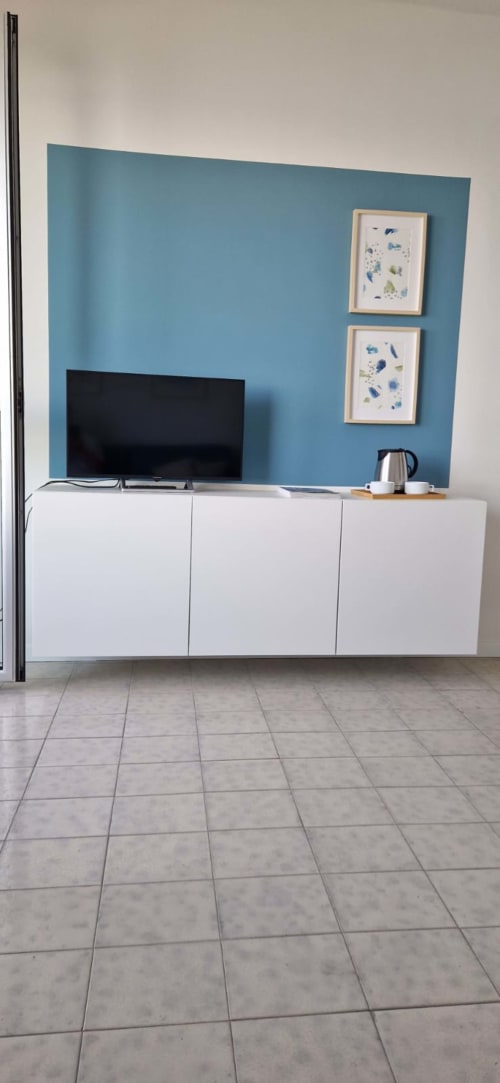 Modern apartment living room with teal accent wall, white media unit, flat-screen TV, and framed botanical art at Lamar