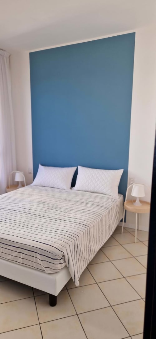 Modern bedroom with blue accent headboard wall, striped bedding, white pillows, and bedside lamps at Lamar Suites Seafront