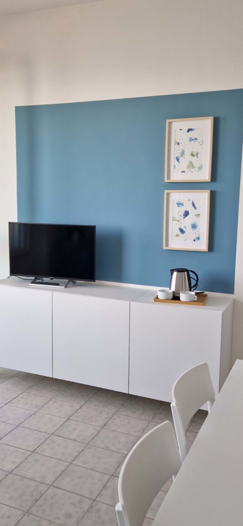 Modern hotel suite entertainment area with blue accent wall, white TV cabinet, flat-screen TV, framed botanical art, and
