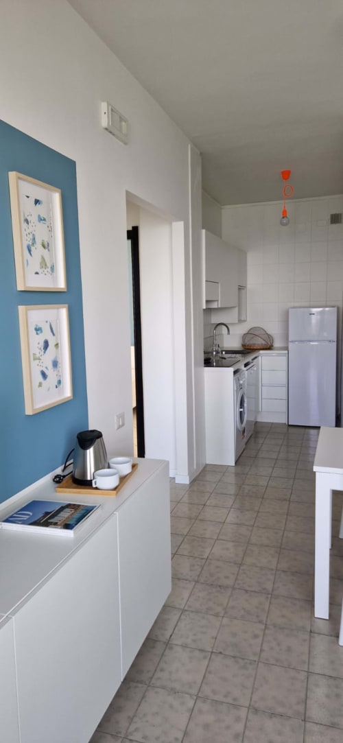 Modern kitchen and hallway in Lamar Suites seafront apartment with blue accent wall, white cabinetry, and stainless steel
