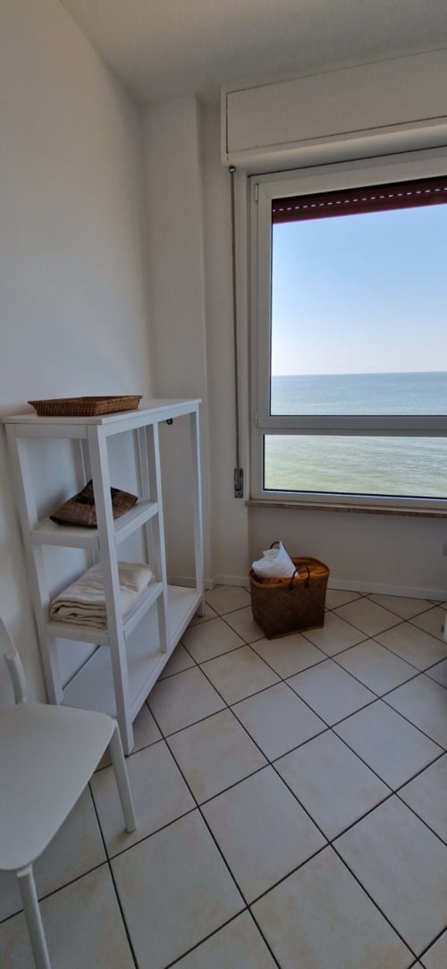 Seafront bathroom with white storage shelves, tile flooring, and sea view through sliding glass door at Lamar Suites, Misano