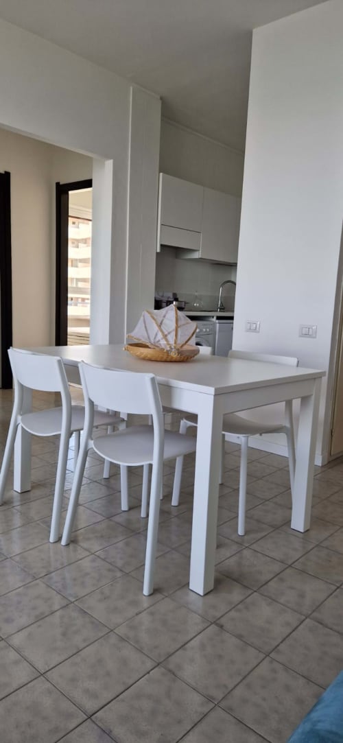 Modern white dining table with chairs in Lamar Suites Seafront apartment, Misano Adriatico, with kitchen and balcony view