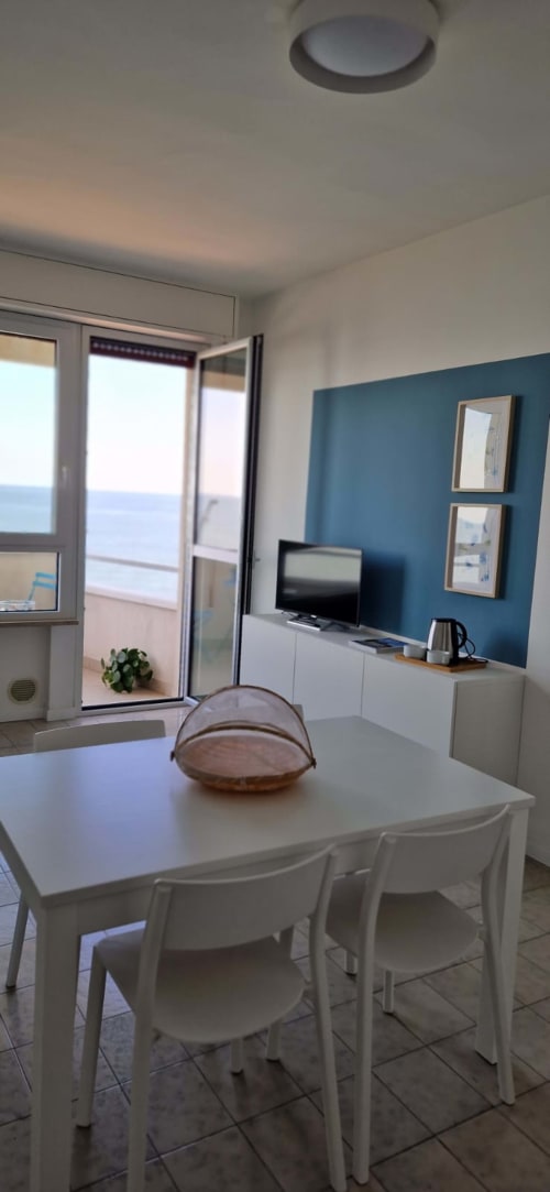 Modern seafront suite in Misano Adriatico with dining table, sea view balcony, TV, teal accent wall, and contemporary