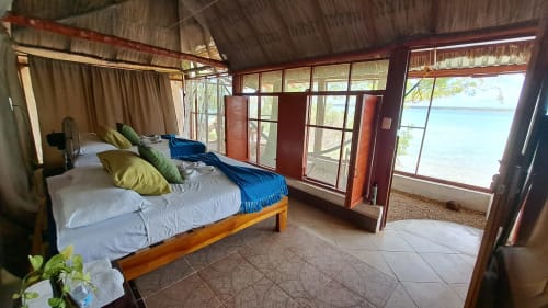 Habitación espaciosa frente al lago en hostel Cayuco Maya, Bacalar, con cama de madera, ropa de cama azul y vistas a la laguna turquesa