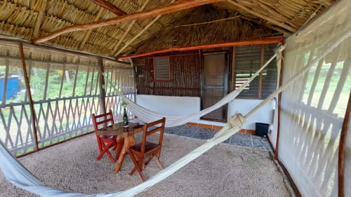 Habitación rústica en Cayuco Maya, Bacalar con hamaca, sillas rojas y vista al lago desde el porche cubierto