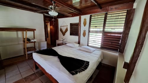 Acogedora habitación en el hostal Cayuco Maya de Bacalar con vigas de madera, paredes blancas y vistas al lago por ventanas con contraventanas