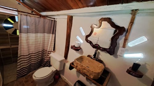 Baño rústico del hostal Cayuco Maya en Bacalar con lavamanos de madera, cortina a rayas y espejo con marco tallado