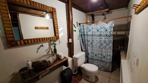 Baño rústico en el hostal Cayuco Maya de Bacalar con acabados en madera, lavabo de piedra y cortina de ducha con patrón azul