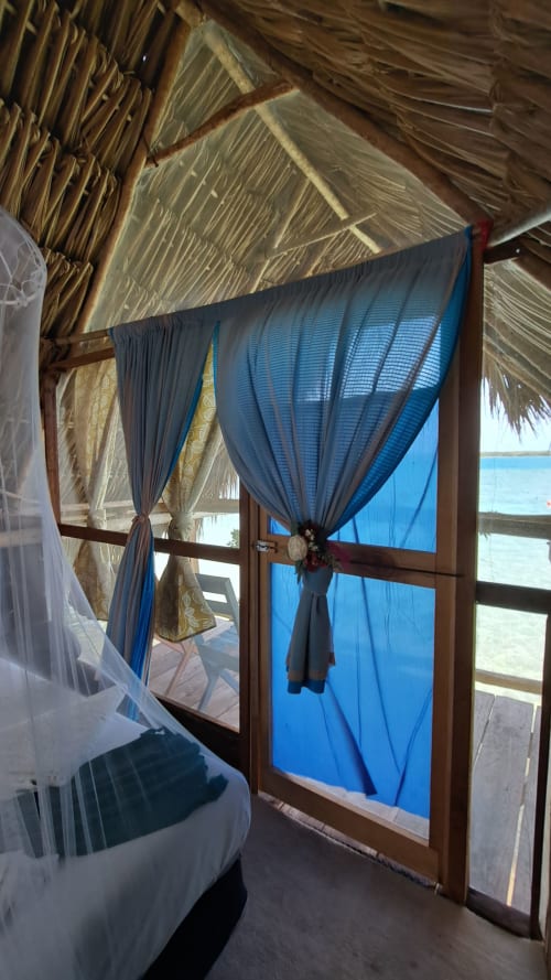 Cortinas azules enmarcan puerta de madera abierta hacia el lago turquesa del hostal Cayuco Maya en Bacalar