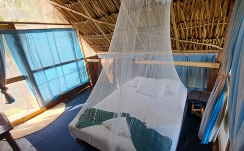 Habitación luminosa del hostal Cayuco Maya en Bacalar con cama de dosel con mosquitero y vista al lago por ventana de persianas azules
