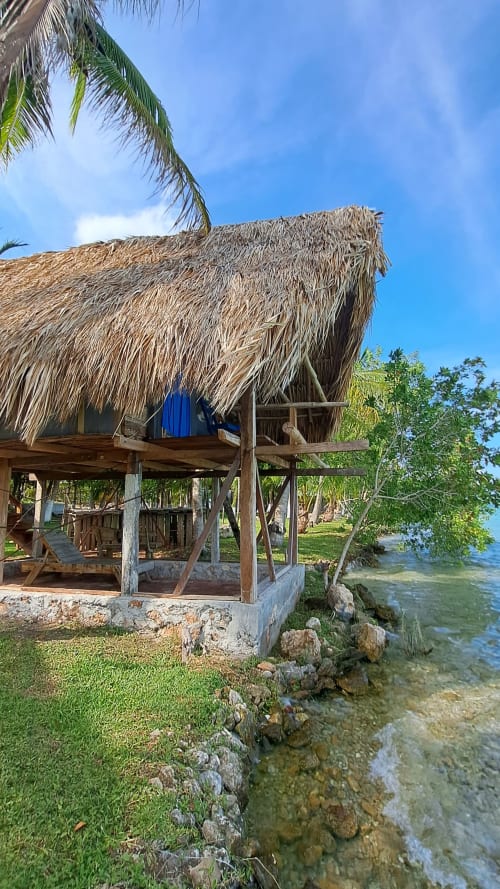 Bungalow con palapa frente al mar en Cayuco Maya hostel, Bacalar, con techo de palma viendo las aguas turquesas del lago