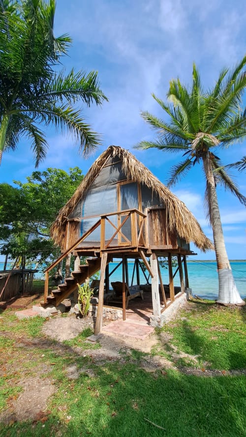 Bungaló con techo de paja en hostal Cayuco Maya, Bacalar, con palmeras y vista al lago turquesa
