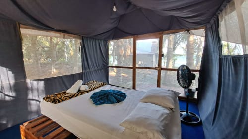 Dormitorio con vista al lago en hostal Cayuco Maya, Bacalar, con cama, ventilador y ventanas de malla con vistas a los árboles