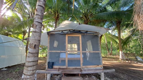 Cabaña con pantalla y puerta de madera en el hostal Cayuco Maya de Bacalar, rodeada de palmeras